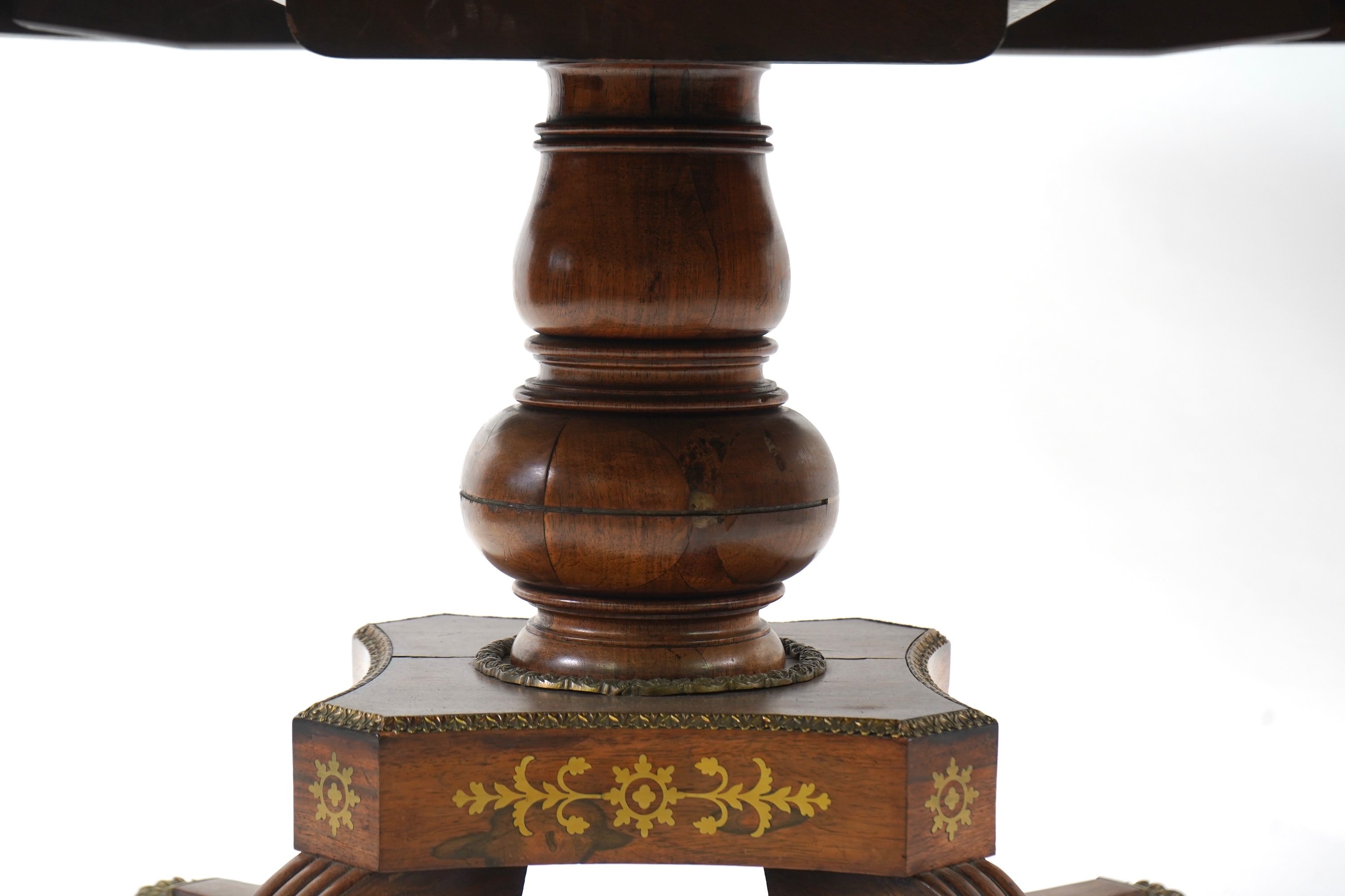 A Regency cut brass inlaid and gilt metal mounted circular rosewood breakfast table, the bird's-eye maple banded tilt top on baluster column, concave platform and quadruple downswept base with cast claw caps and castors,